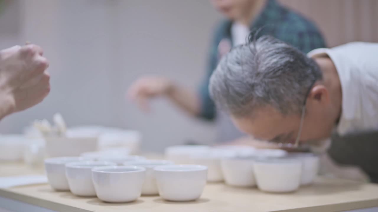 3名亚洲华裔男咖啡师品酒师表演杯咖啡，品尝杯咖啡后在剪贴板上写下视频素材
