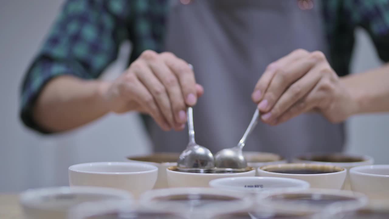 亚洲华人男咖啡师铲咖啡渣，为咖啡杯品尝范围，从桌上的陶瓷杯子上撇去咖啡渣视频素材
