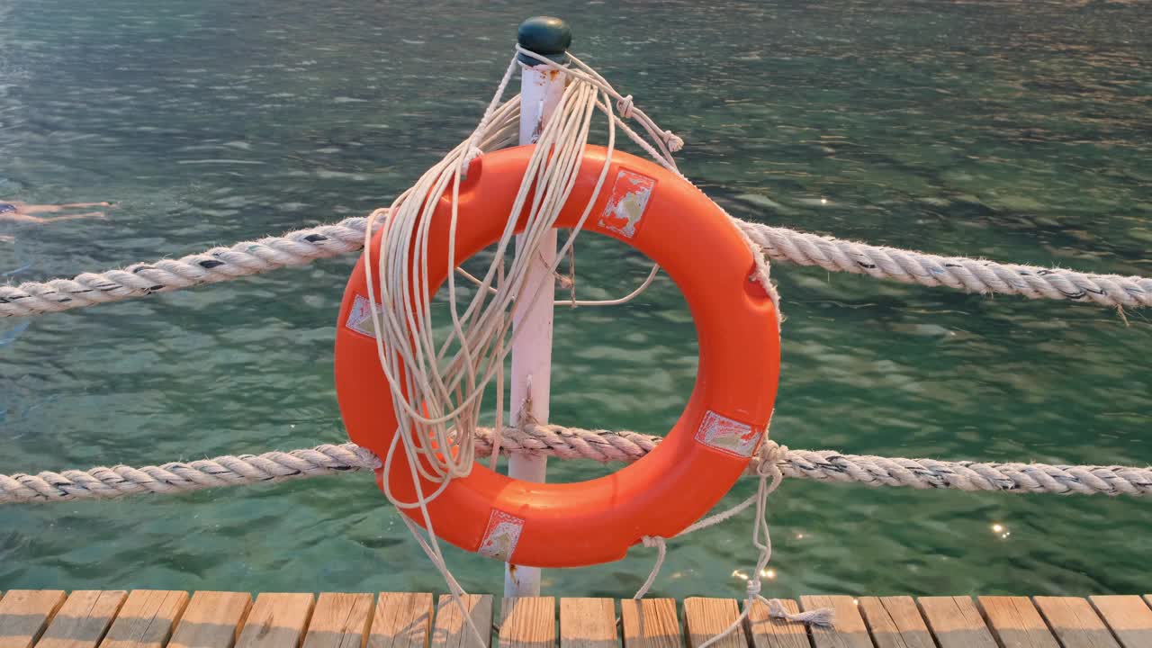 橙色的生命线和海绳在大海和蓝天的背景上。挂在一根柱子上的海缆和救生圈。救助和安全概念视频下载