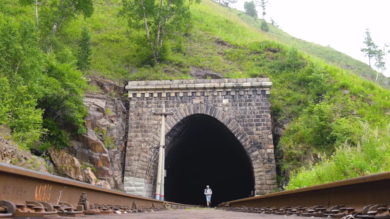 一名背着背包的男性游客从隧道沿着铁轨走出来。视频下载