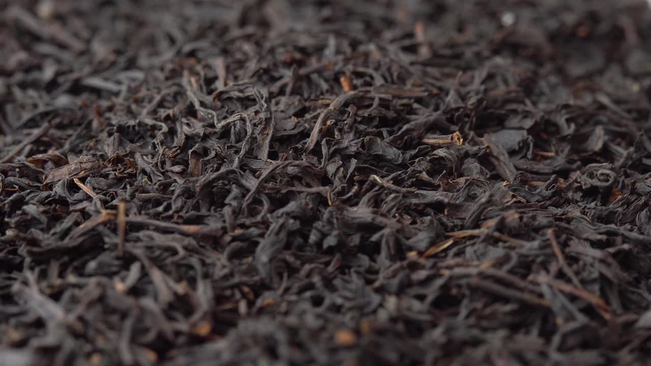 黑色散叶茶叶洒在盘子上并旋转特写，背景为咖啡馆或餐厅的茶叶广告视频下载