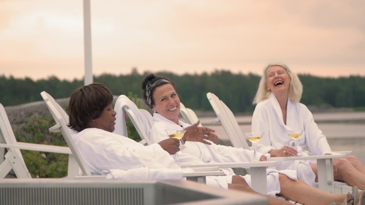开朗的多种族资深女性朋友在日落时坐在甲板椅子上喝酒视频下载