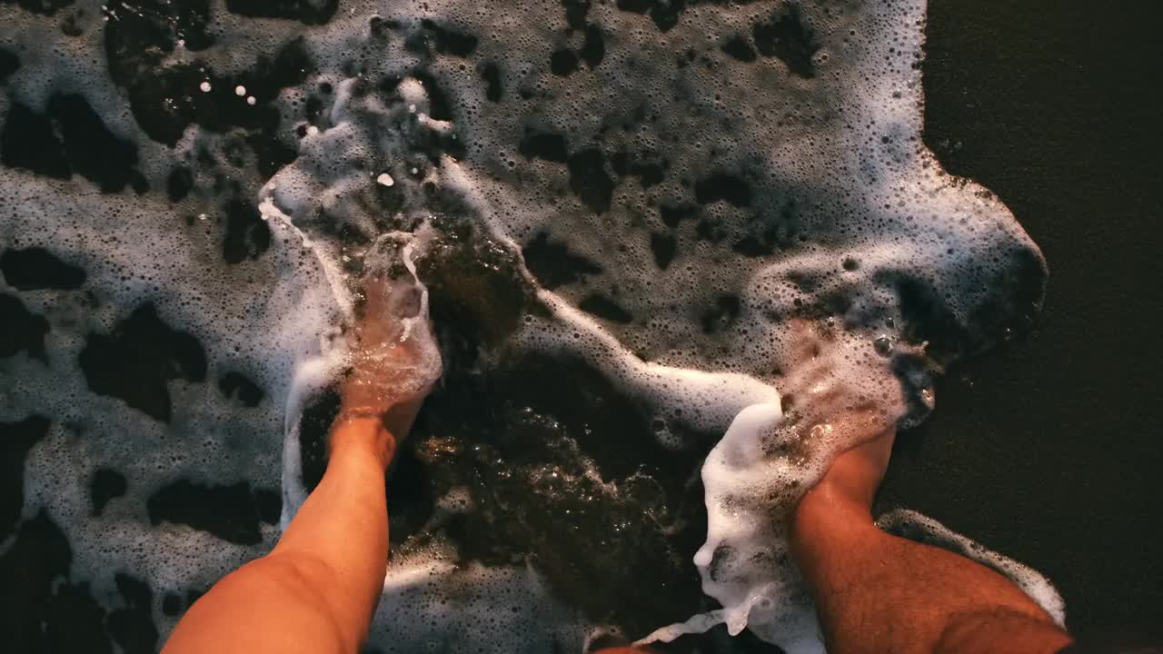 情侣们在沙滩上散步，他们的脚踩在海浪和沙子上。视频素材