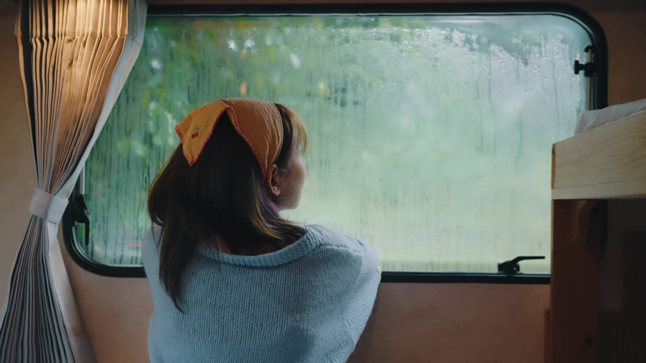 孤独的女人透过窗户看着雨。视频购买