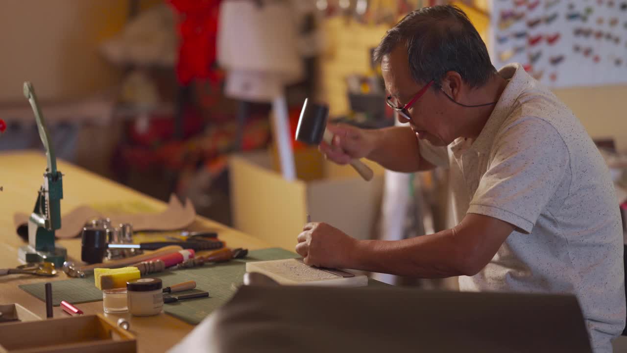 一位亚洲华人老人在他的工作室里制作手工皮革表带视频下载