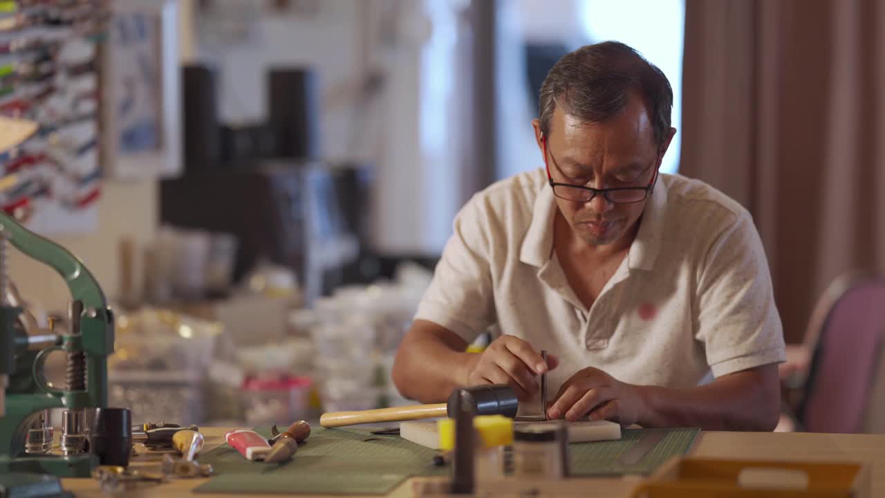 一位亚洲华人老人在他的工作室里制作手工皮革表带视频下载
