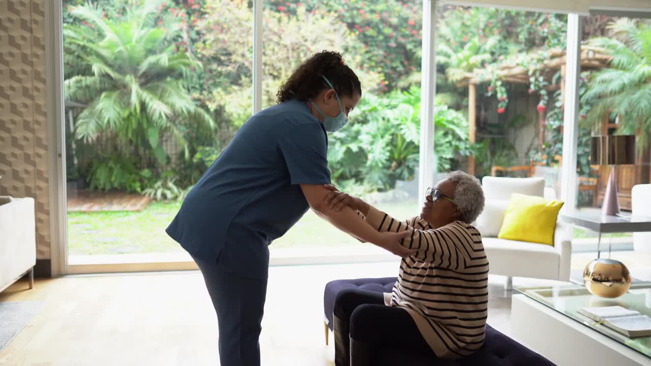 家庭护理人员帮助一位老年妇女站在家里-医生戴着防护口罩视频下载