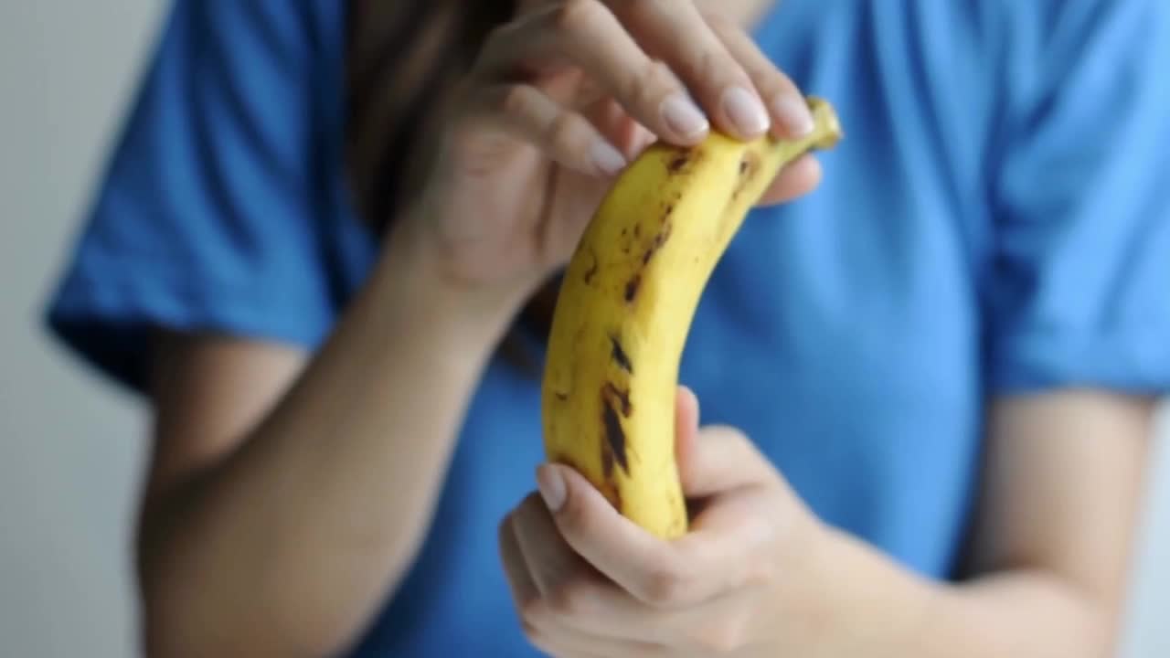 一位身着休闲装的东南亚妇女正在剥一根熟透的香蕉视频下载