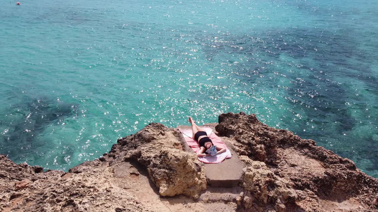 一个女人在碧绿的大海附近的一块岩石上休息视频下载