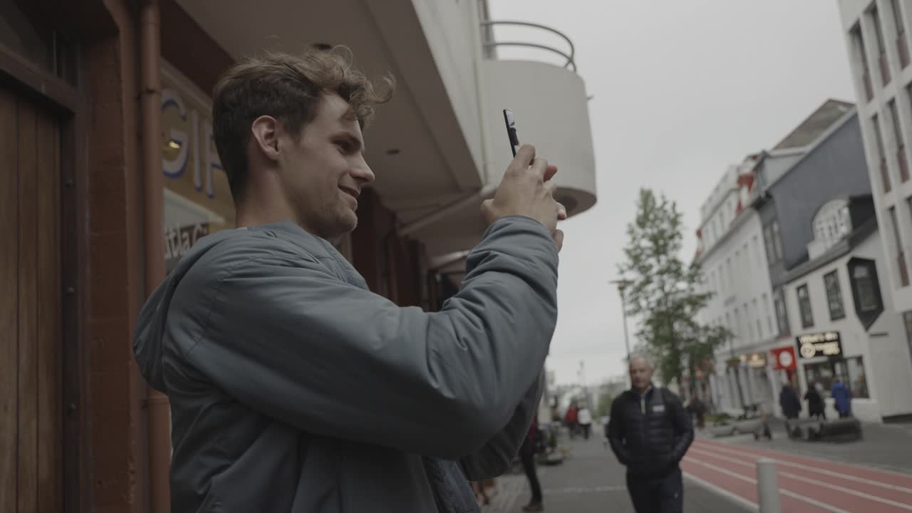 冰岛，雷克雅未克，一名男子在给街对面查看手机的女子拍照视频素材