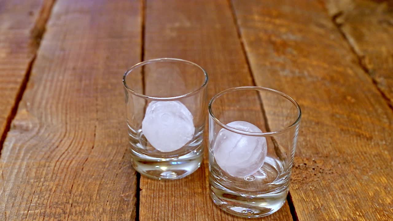 将酒精饮料倒在一个透明玻璃杯的冰球或球上。视频下载
