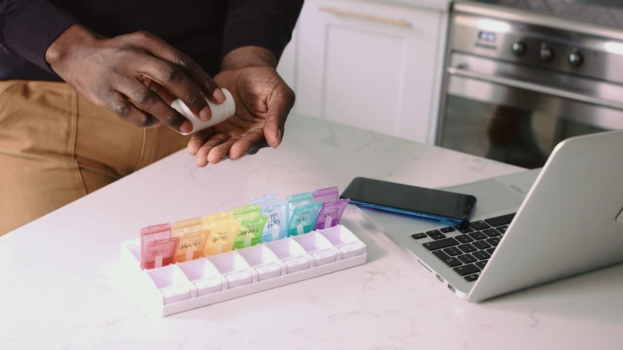 特写的黑人男子的手把处方药放在一个每日药片整理视频素材