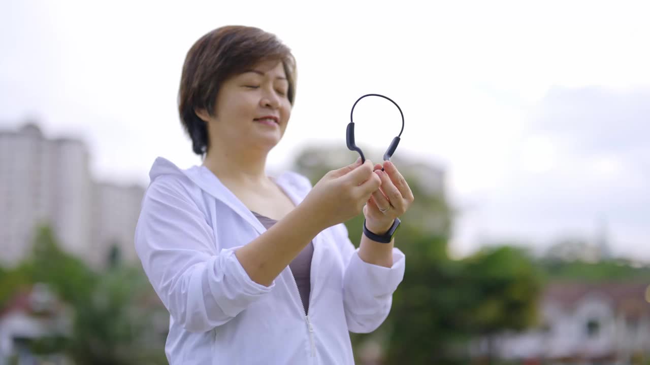 亚洲华人中年女性，穿着运动服，戴着耳机，微笑着跑向公园视频素材