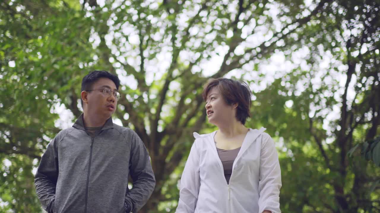 亚洲华人中年夫妇，穿着运动服，在公园散步，聊天，微笑视频素材