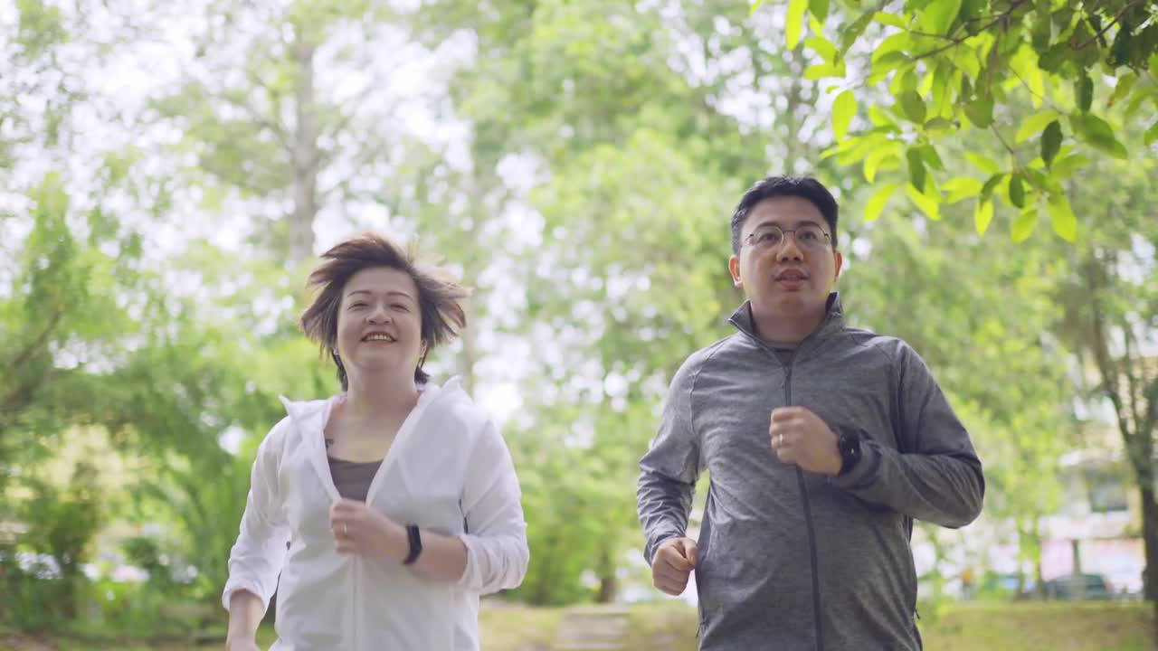 亚洲华人中年夫妇穿着运动服跑着微笑着看向公园视频下载