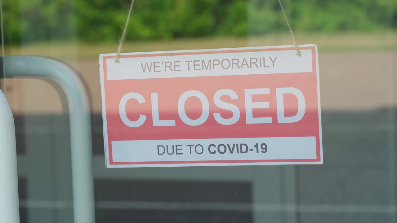 一名男子摘下挂在透明门上或店面前的“2019冠状病毒病大流行期间关闭”的标志视频素材