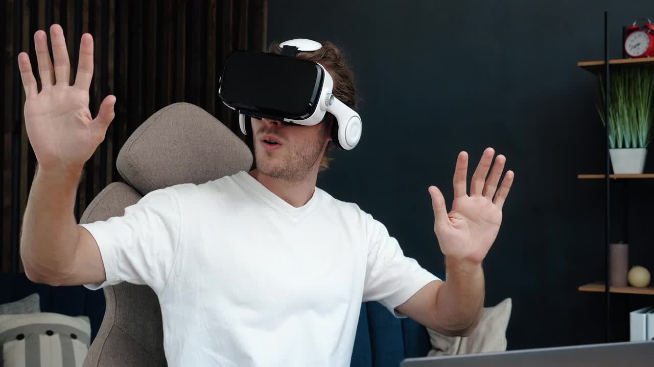 英俊的白人男子兴奋地戴着虚拟现实耳机在家里。增强现实。男人在室内用现代3D VR眼镜触摸东西。学生在家玩眼镜。拍摄4 k。视频下载