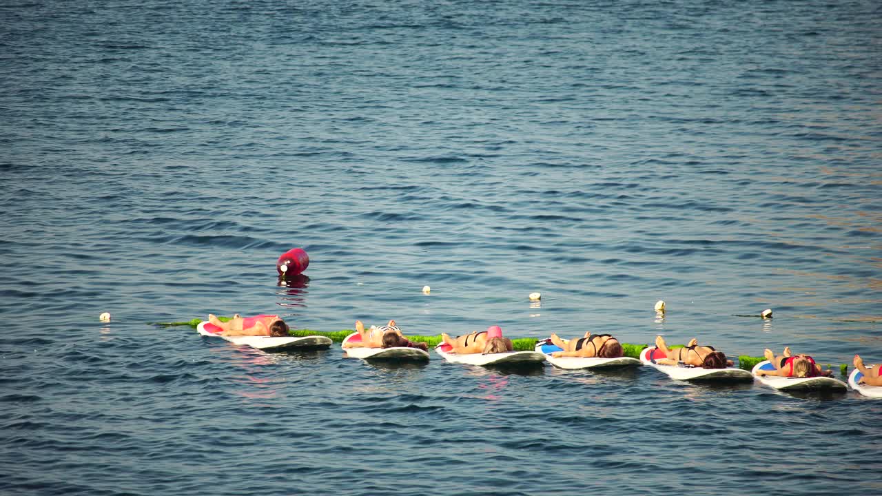 清晨，一群穿着泳衣的年轻女子在平静的海面上做瑜伽和普拉提。平衡姿势-健康生活和身心发展之间的自然平衡的概念视频素材