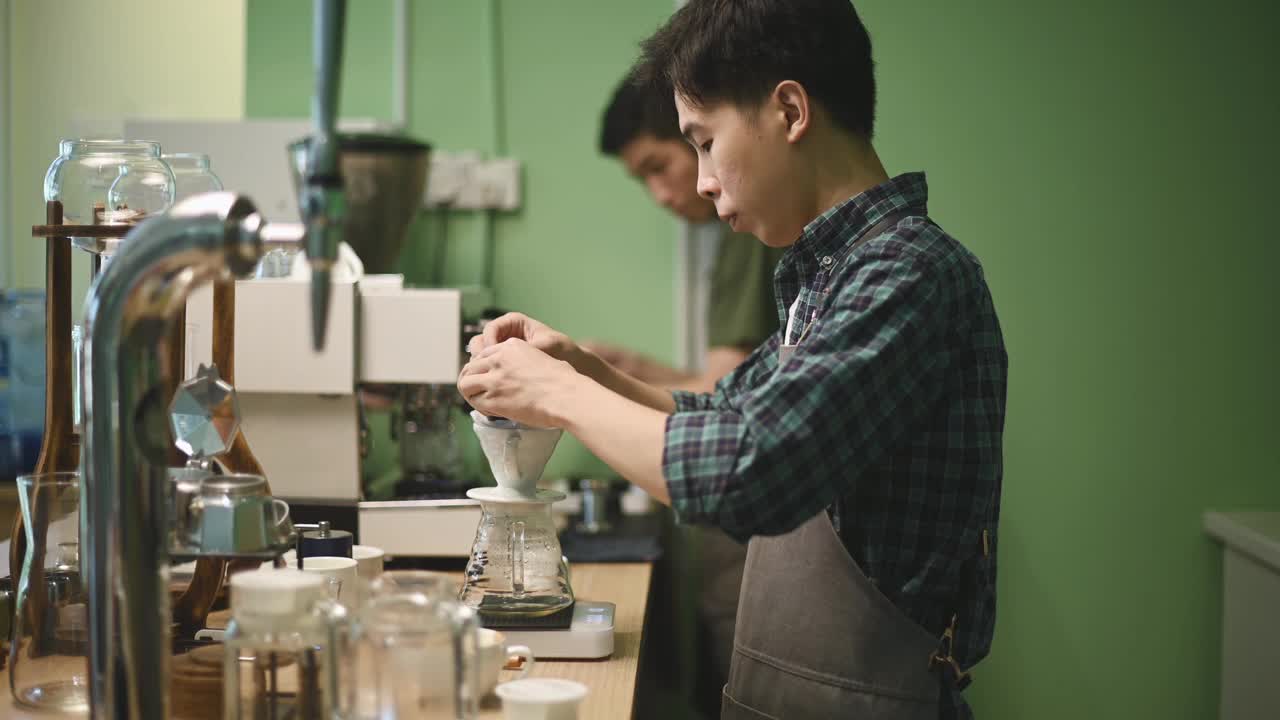 亚洲华人男咖啡师手把咖啡粉倒在咖啡过滤器上，让咖啡滴在咖啡里视频下载