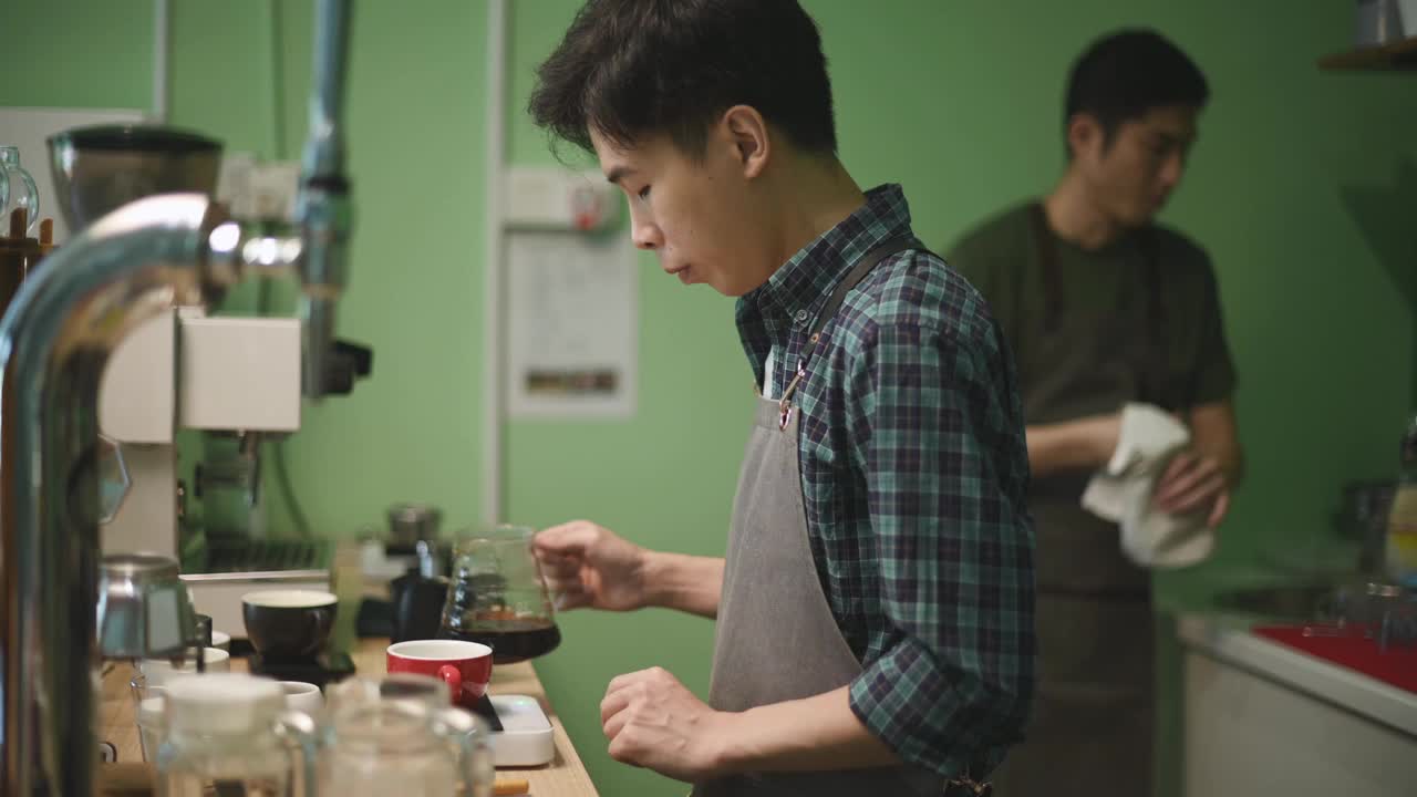 亚洲华人男咖啡师用手将煮好的咖啡从咖啡壶倒入陶瓷咖啡杯视频下载