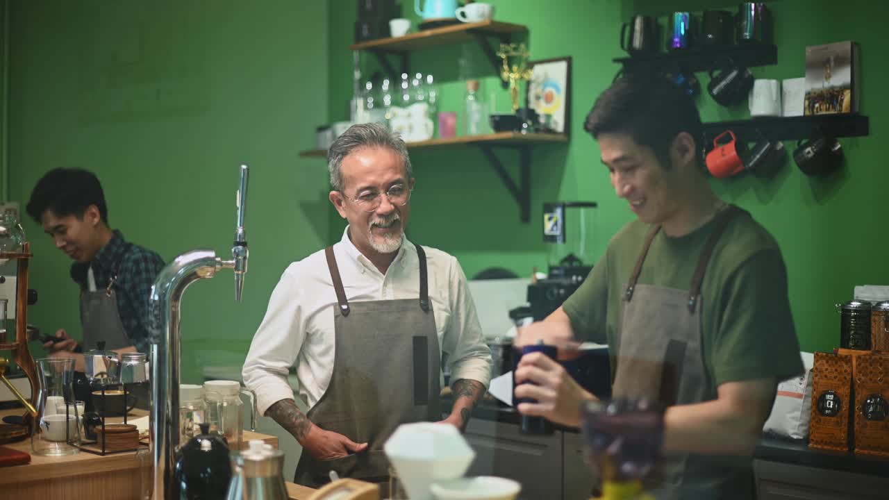 亚洲华人资深男咖啡师老板喜欢和在吧台磨咖啡的员工聊天视频素材