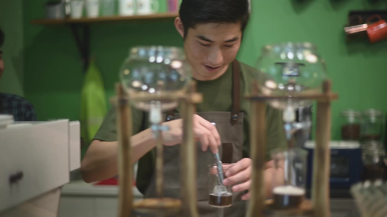 亚洲华人男咖啡师在咖啡店准备冰滴咖啡，加入冰块视频素材