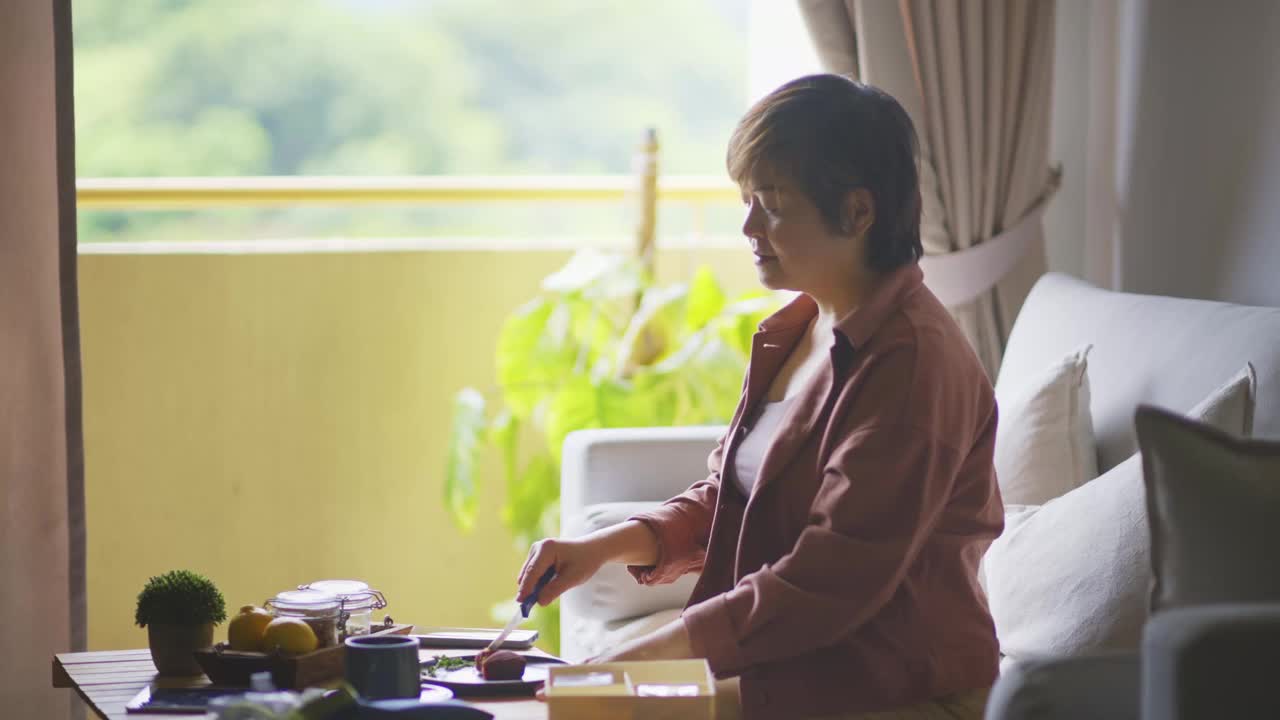 亚洲华人女子在客厅切雪皮月饼，享用中国传统节日甜点的下午茶视频素材