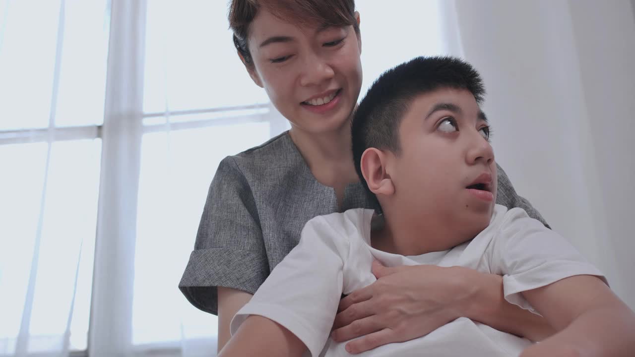 亚洲女性母亲，看护者或理疗师在家中拉伸和锻炼残疾男孩12岁。家庭物理疗法视频素材