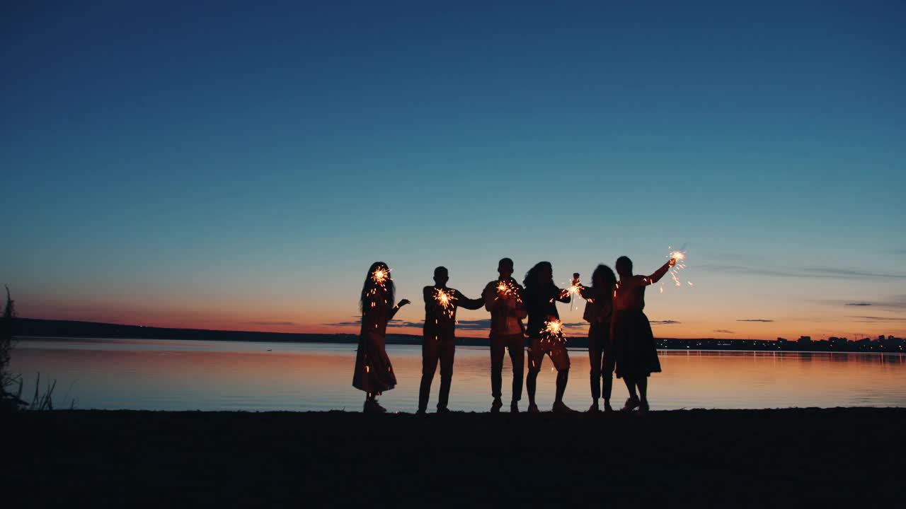 一群年轻的朋友在湖边跳舞，火花在深夜视频素材