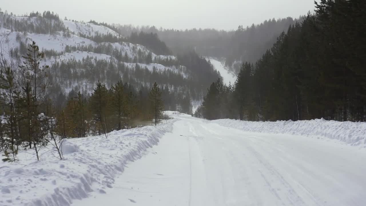 在多云的冬日，山坡上冬季道路的景象。镜头。一场暴风雪在一个冬天的老采石场的小路上的第一人称视角视频下载