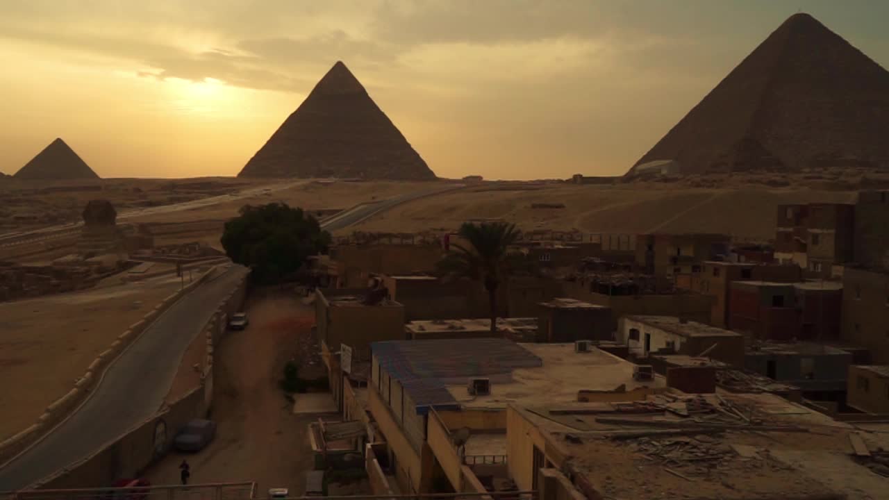 埃及开罗吉萨附近的狮身人面像和吉萨大金字塔(胡夫金字塔，哈夫拉金字塔和Menkaure金字塔)的日落景观视频下载