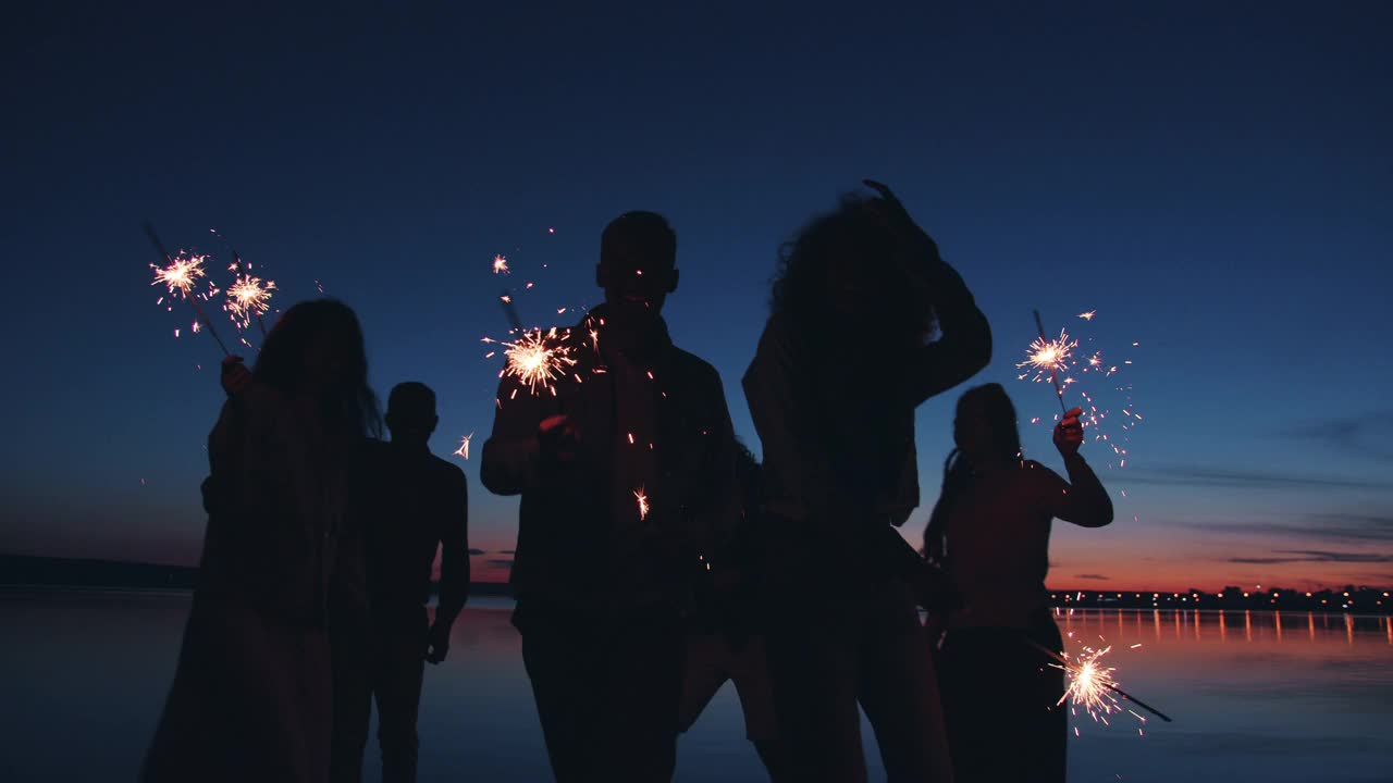 夜晚的湖岸上，男人和女人的剪影拿着烟花翩翩起舞视频素材