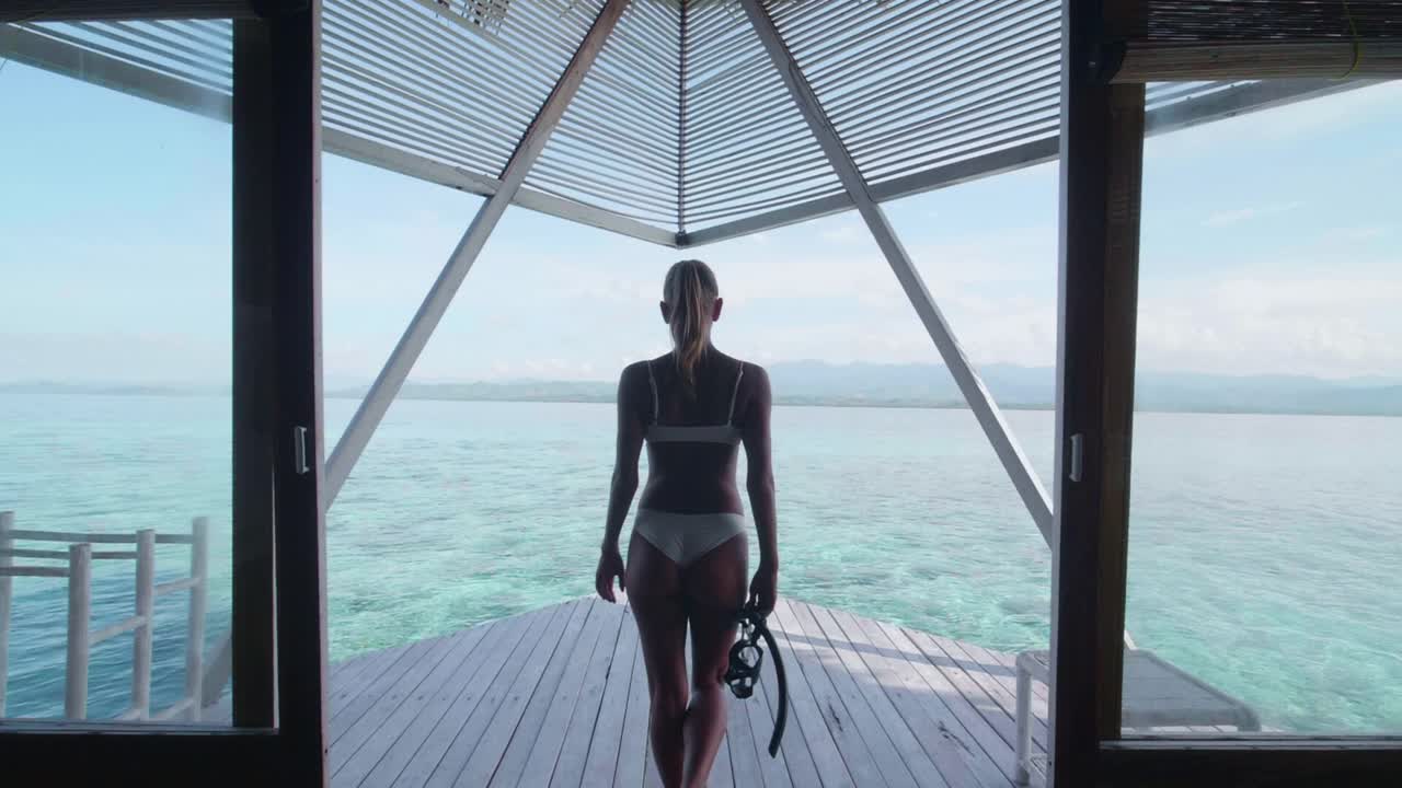 比基尼泳装穿着泳装的女子走到阳台甲板上的一个热带岛屿酒店度假村。——慢动作视频素材