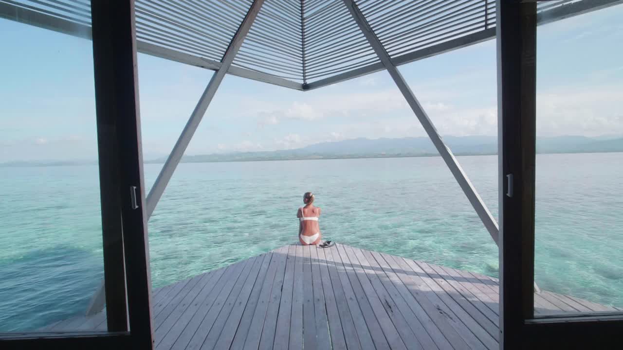 比基尼泳装穿着泳装的女子坐在热带岛屿度假酒店的阳台甲板上。——慢动作视频素材