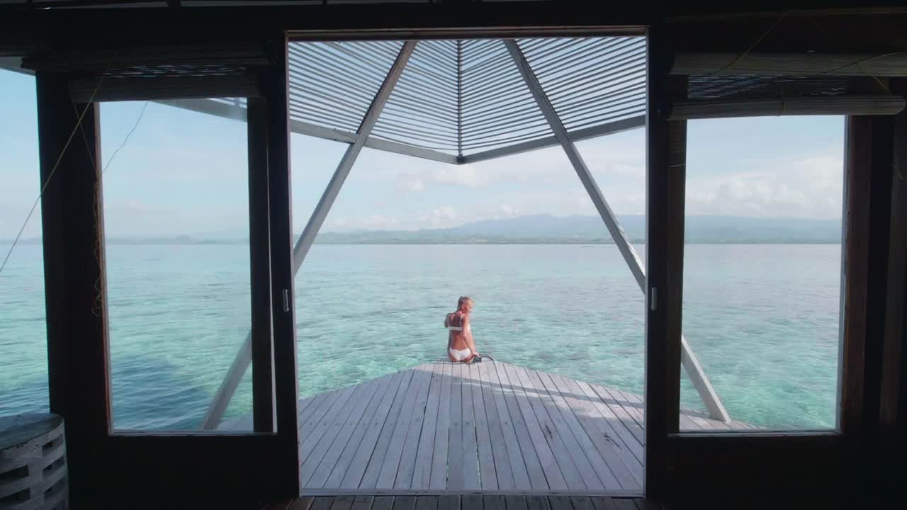 比基尼泳装穿着泳装的女子坐在热带岛屿度假酒店的阳台甲板上。——慢动作视频素材