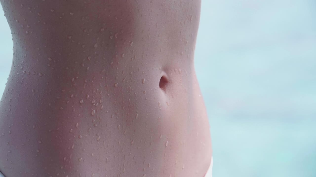 女人腹部平坦，腹部湿漉漉的，是游泳时穿的比基尼泳装。——慢动作视频素材