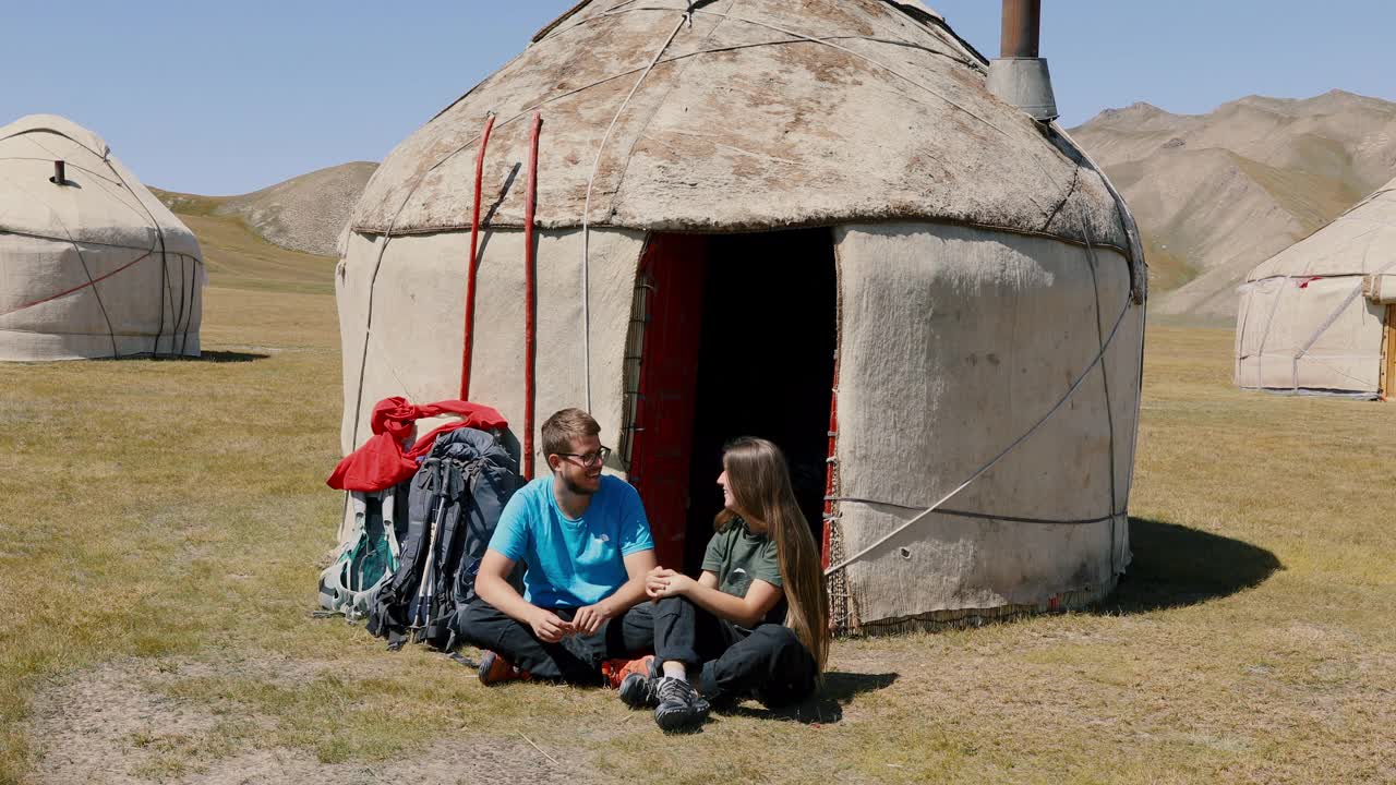 年轻的男女背包客早上在吉尔吉斯斯坦的蒙古包营地相遇视频下载