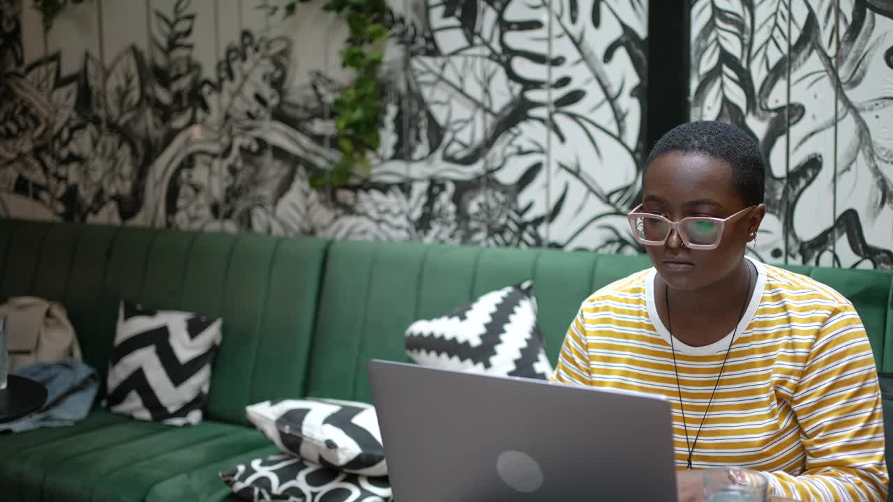 年轻女子一边在咖啡馆用笔记本电脑工作一边用智能手机视频下载