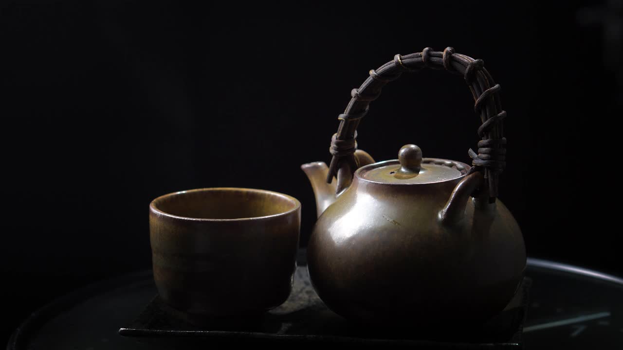 将热茶倒入玻璃茶壶和杯子中，木制背景上有蒸汽。健康热茶概念视频下载