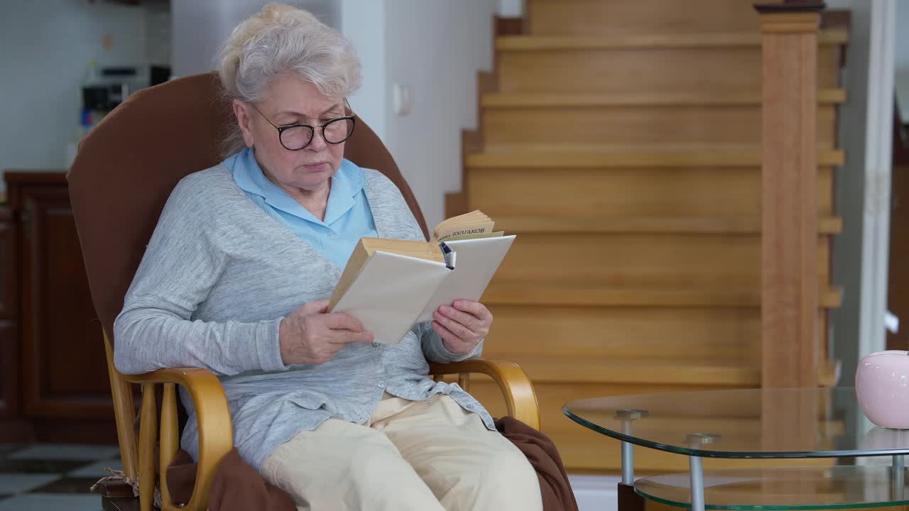 白头发美丽的白种人女人的肖像看书，脱下眼镜，摩擦眼睛。轻松的女退休老人在家里的客厅里享受着闲暇。退休和生活方式视频素材