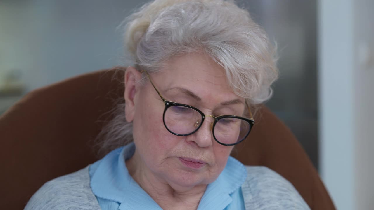 特写的美丽的白种老年女性退休脱下眼镜擦眼睛。一个头发花白的女人坐在家里舒适的扶手椅里视频素材