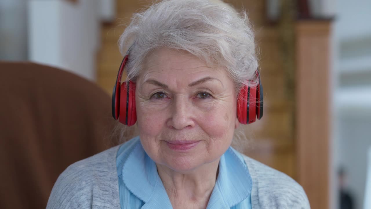 快乐无忧无虑的老女人头照看着相机随着音乐跳舞。特写照片，开朗轻松的白人退休享受爱好在家里微笑视频素材