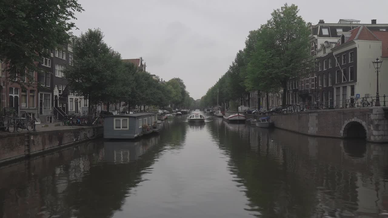 在阿姆斯特丹沿着运河的步行街和桥上，在恶劣的天气里，有一艘游船视频素材