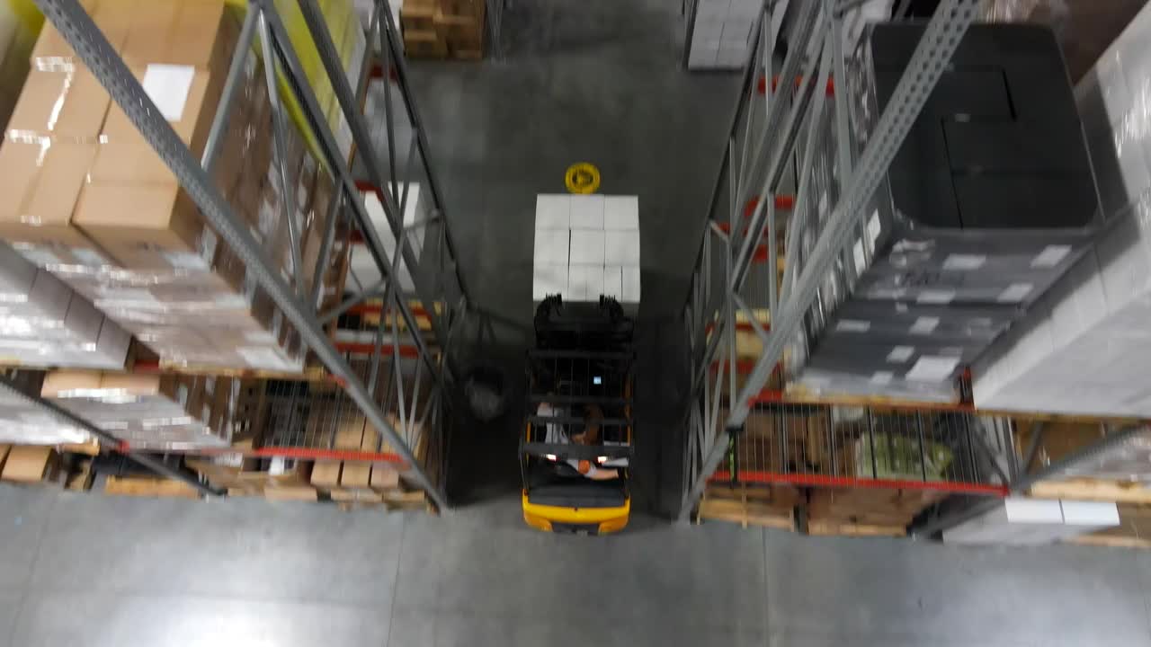 高空拍摄的仓库工人用叉车在仓库的通道角落向后移动货物托盘视频素材