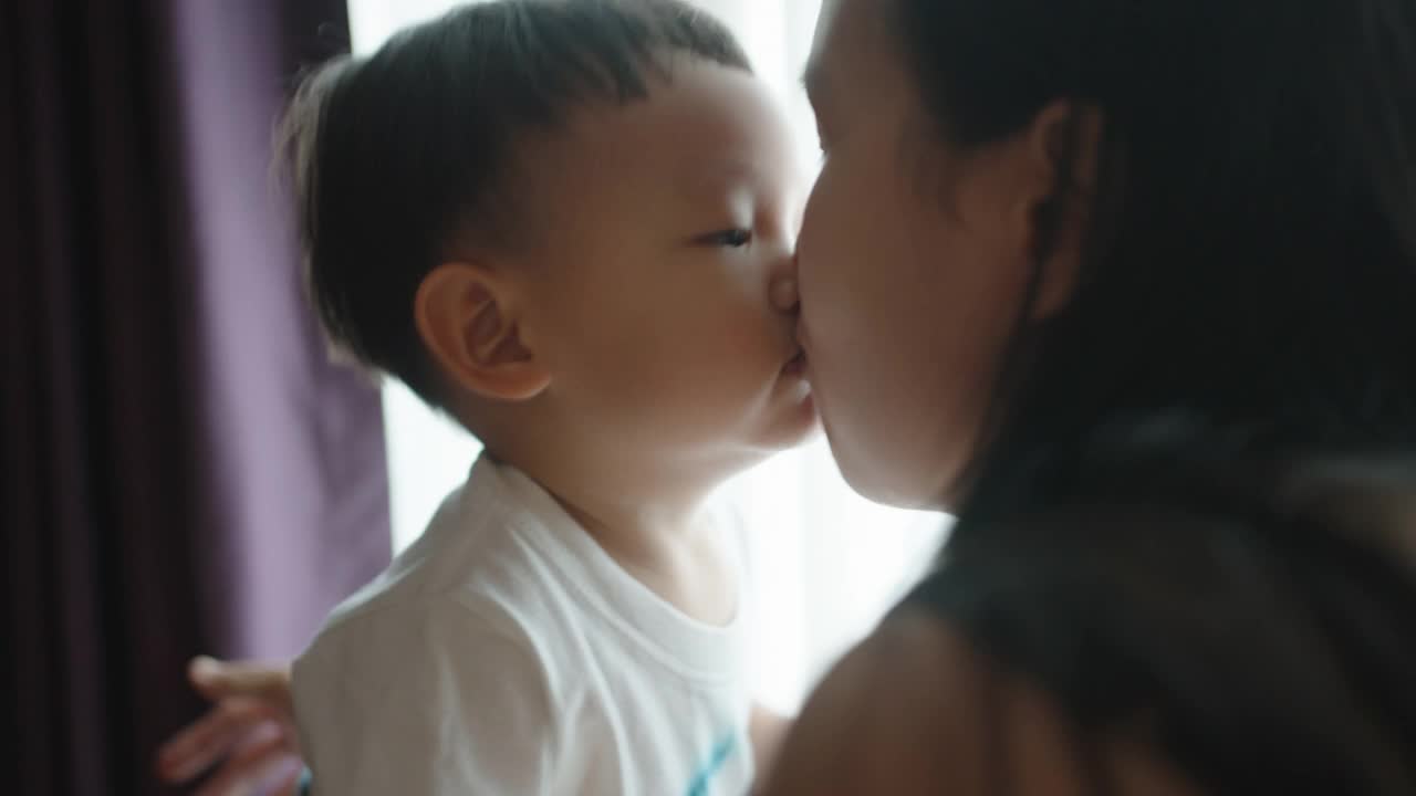 在家里的卧室里，男婴亲吻着他怀孕的母亲的肚子视频素材