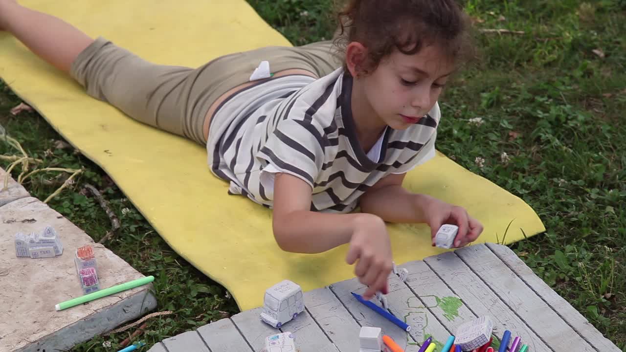小女孩躺在草坪上的黄色垫子上，给一辆玩具汽车上色视频下载