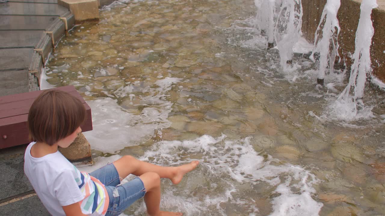 在一个炎热的日子里，一个孩子在公园里的城市喷泉的水里散步。视频素材