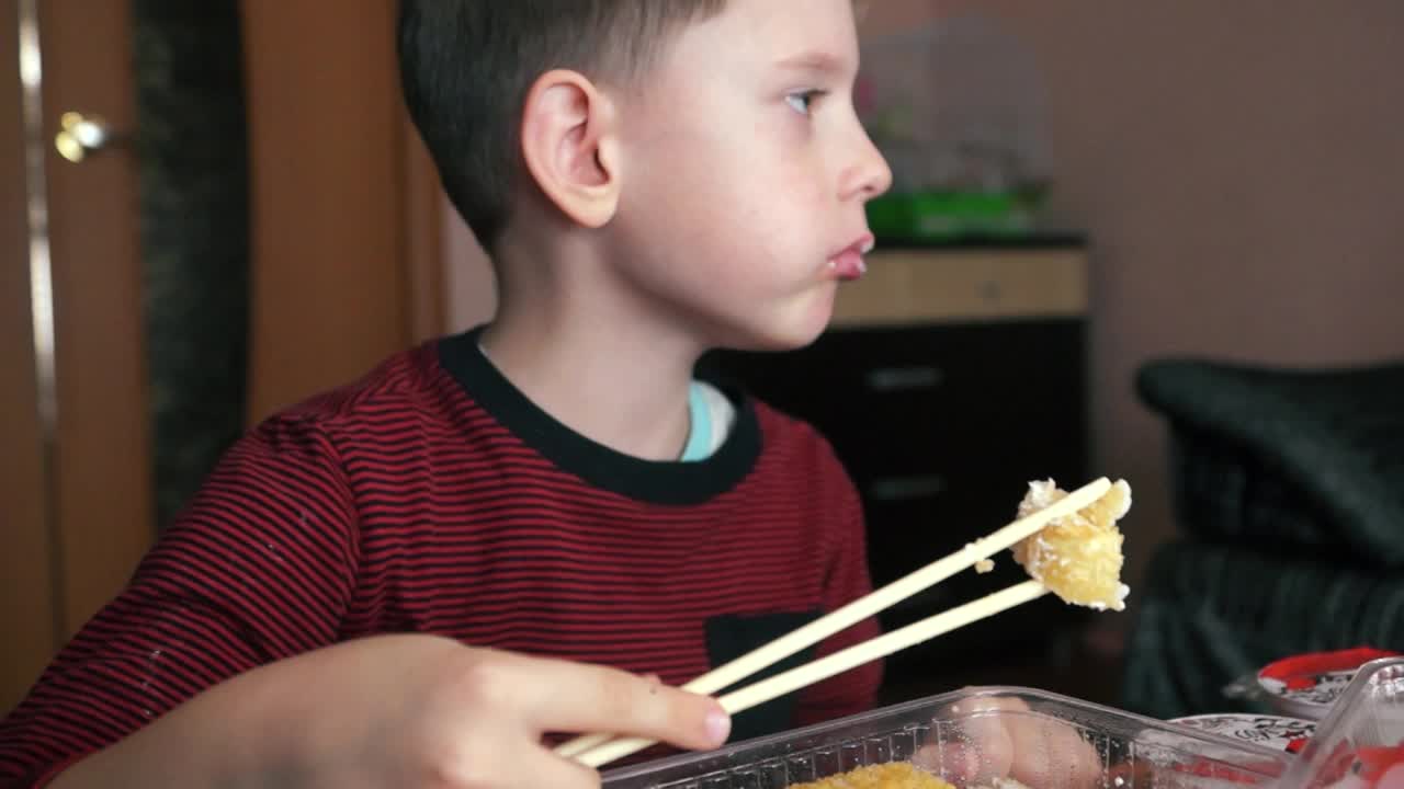 白种学前班男孩愉快地用筷子吃开胃寿司。孩子正在吃日本寿司。寿司外卖和准备。选择性聚焦，浅景深视频素材