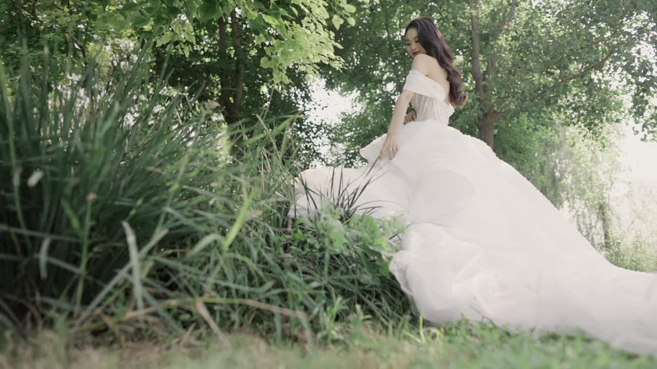 年轻的亚洲女孩穿着白色的长尾婚纱，对着镜头微笑，幸福的新娘视频下载