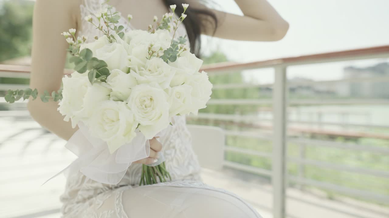 一个美丽年轻的亚洲新娘，手里拿着白色的鲜花，对着镜头微笑，中国新娘视频素材